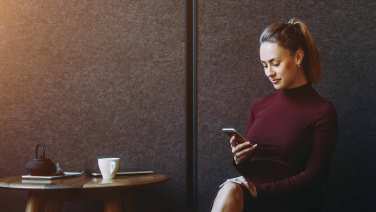 Giovane ragazza seduta in un caffè opera sul suo home banking da smartphone.