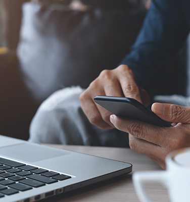 Mano di un uomo che digita sul cellulare davanti a un computer.