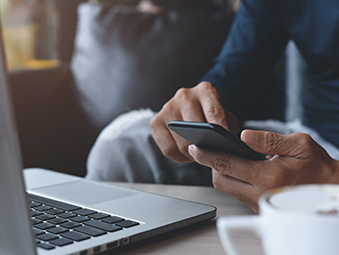 Mano di un uomo che digita sul cellulare davanti a un computer.