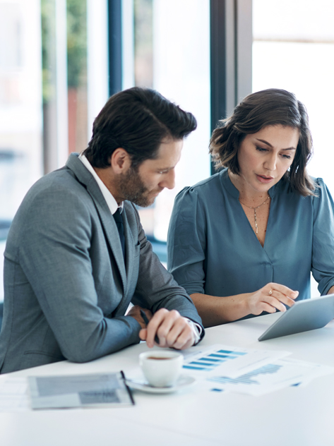 Due professionisti che discutono report finanziari in ufficio con documenti sul tavolo.