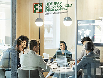 Un gruppo di gestori discute le scelte di investimento in una sala riunioni. Sul vetro il logo di Fideuram Asset Management